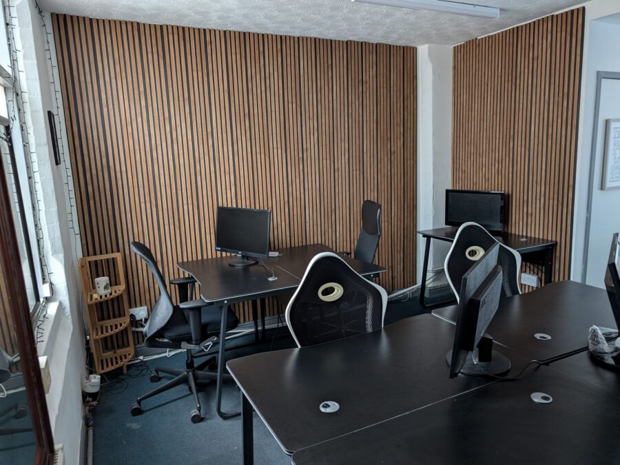 Desks with monitors and office chairs beside the wooden slat wall